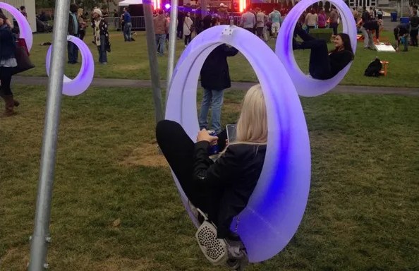 Illuminated swings on a lawn at dusk, with people sitting in them